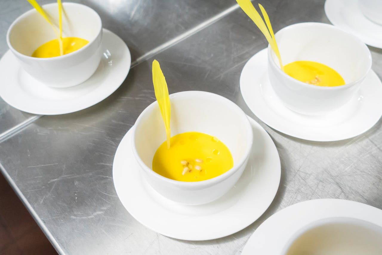 heros-img A high-angle view of creamy yellow soup garnished in elegant white bowls, exuding a modern culinary presentation.
